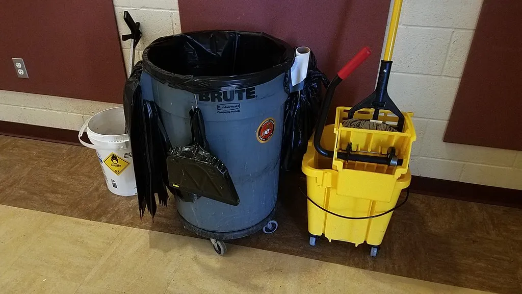 A commercial cleaning trolley with a mop bucket, bin and mop